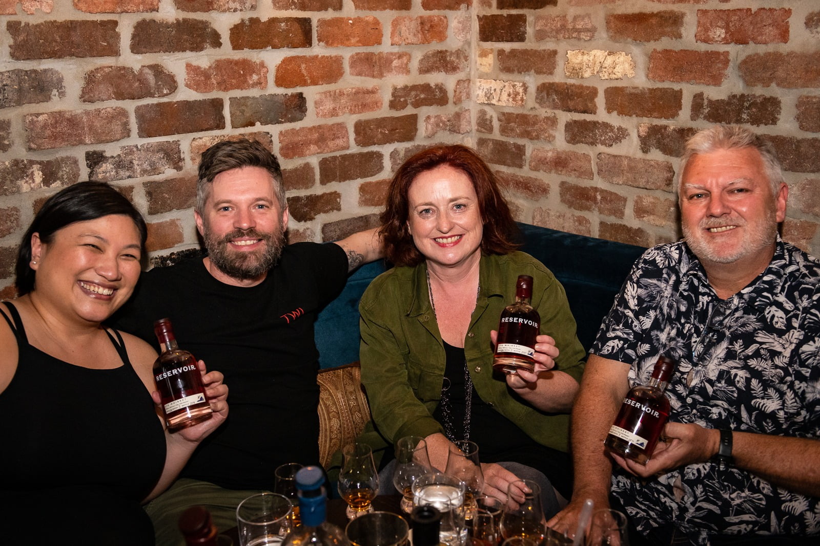 Happy group of whiskey aficionados smiling and holding up mini bottles of Reservoir whiskey